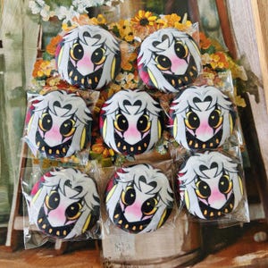 May include: A collection of round plush toys featuring a cartoon owl design. The owls have white and gray hair, yellow eyes, and a pink blush. The toys are packaged in clear plastic.