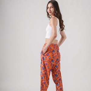 Handmade cotton pajama bottoms featuring colorful blue and purple flowers on bright orange fabric – soft, comfy, and breathable sleep pants designed with elastic waist, drawstring closure, and spacious side pockets, ideal for floral print clothing lovers, gifts for flower lovers, book lovers, and stylish cotton gift ideas.