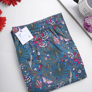 Relaxed fit printed lounge bottoms in breathable cotton, featuring bright pink butterflies and floral design on blue fabric, elastic waist, drawstring, and handy side pockets.
