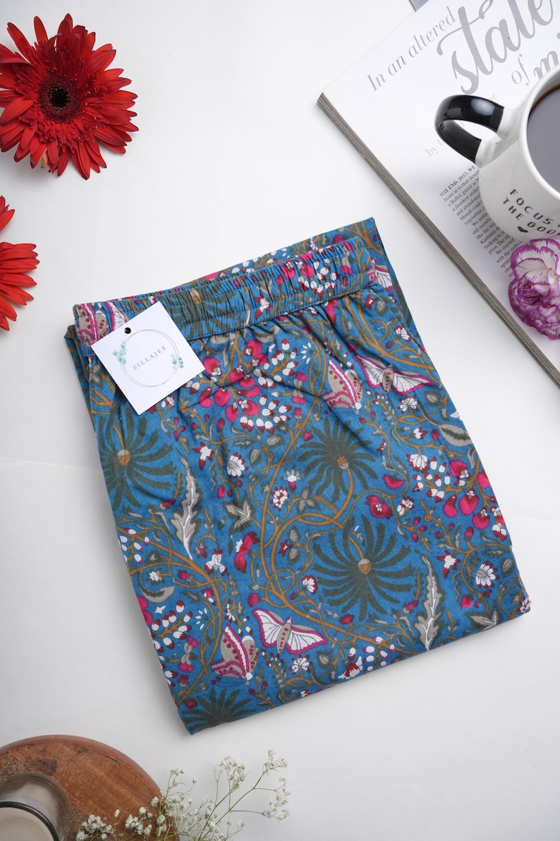 Relaxed fit printed lounge bottoms in breathable cotton, featuring bright pink butterflies and floral design on blue fabric, elastic waist, drawstring, and handy side pockets.