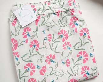 May include: White cotton pajama pants with a pink and green floral print. The pants have an elastic waistband and a tag that says "Zillatee".