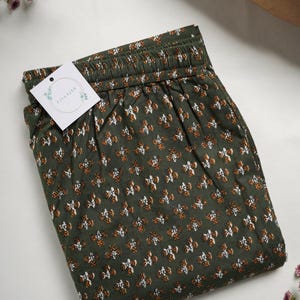 May include: Green cotton shorts with a white and orange floral print. The shorts have an elastic waistband and a tag that says "Killager".