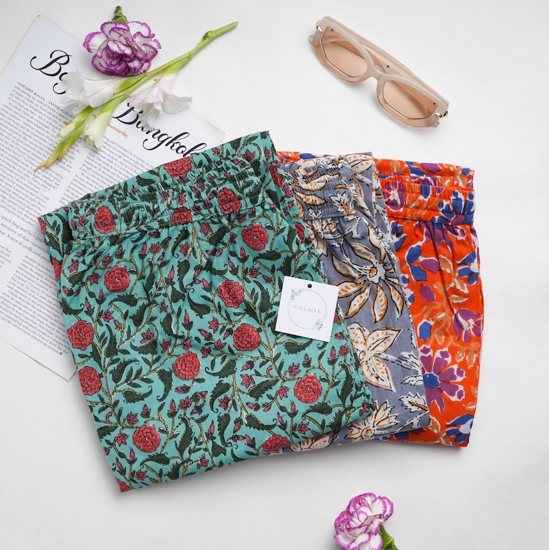 Set of 3 handmade 100% cotton pajama pants for women in vibrant floral prints of gray, orange, and green – relaxed fit jammies with elastic waistband, adjustable drawstring, and deep side pockets, perfect as breathable, lightweight lounge & sleepwear or thoughtful menopause gift ideas and cotton anniversary presents for flower or book lovers.