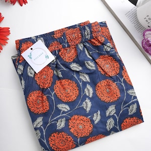 May include: A pair of blue cotton pajama pants with a floral print. The print features orange flowers with white accents on a navy blue background. The pants have an elastic waistband and a tag that says "Zillajee".