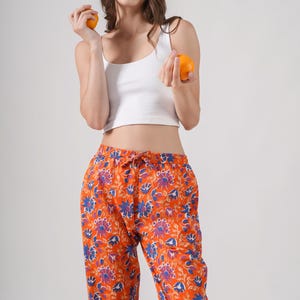 Vibrant 100% cotton pajama pants for women with striking blue and purple floral prints on a bold orange base – breathable, lightweight lounge pants with elastic waistband, adjustable drawstring, and functional pockets, perfect as relaxed fit pj pants, trendy sleep trousers, or unique menopause gift ideas and cotton anniversary gifts.