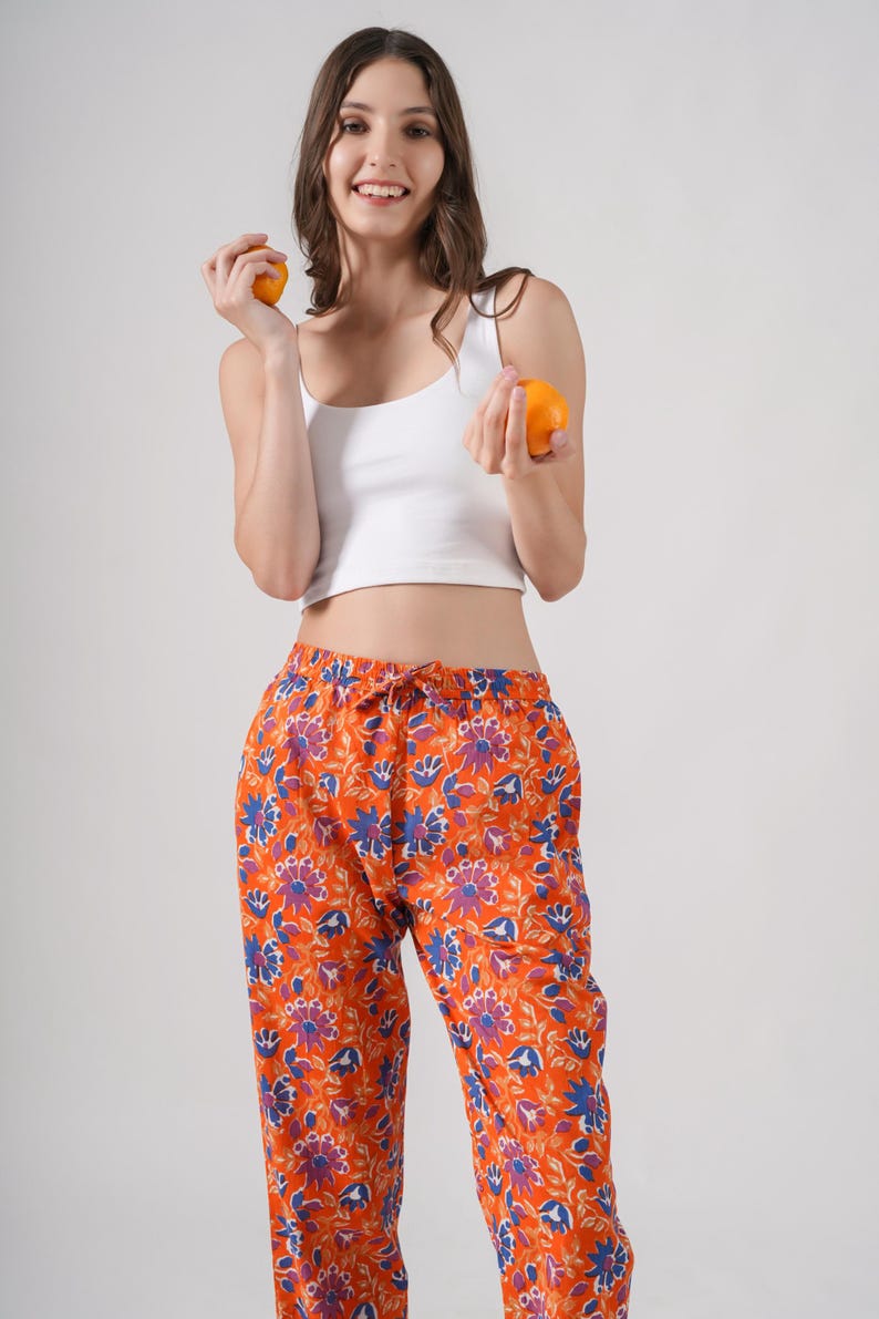 Vibrant 100% cotton pajama pants for women with striking blue and purple floral prints on a bold orange base – breathable, lightweight lounge pants with elastic waistband, adjustable drawstring, and functional pockets, perfect as relaxed fit pj pants, trendy sleep trousers, or unique menopause gift ideas and cotton anniversary gifts.