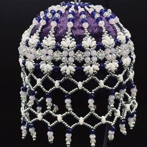 Könnte beinhalten: Handgefertigter, kugelförmiger Schmuck mit tiefvioletter Samtbasis. Der Schmuck ist mit aufwendigen Perlenarbeiten in Weiß, Silber, Hellrosa und Dunkelblau verziert. Der Text "Winter Chill" wird unten angezeigt.