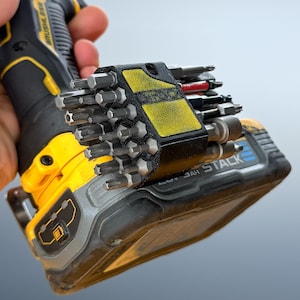 May include: A black and yellow cordless drill with a bit holder attached, filled with various screwdriver bits. The drill has the word "BRUSHLESS" printed on it. The bit holder has yellow accents.