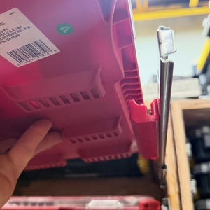 K&ouml;nnte beinhalten: Ein rotes Kunststoff-Aufbewahrungselement mit einem seitlichen Metall-Gleitschienenmechanismus. Auf der Oberfl&auml;che befindet sich ein wei&szlig;es rechteckiges Etikett mit Strichcode und Text sowie ein kleiner gr&uuml;ner, runder QC PASS-Aufkleber.