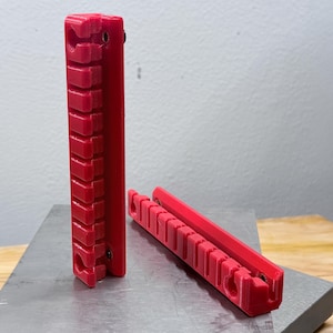 K&ouml;nnte beinhalten: Zwei leuchtend rote, l&auml;ngliche Kunststoff-Organizer mit einer Reihe von zehn gleichm&auml;&szlig;ig verteilten, kreisf&ouml;rmigen Clips an einer Seite. Jeder Organizer hat eine flache R&uuml;ckseite und eine vertikale Reihe offener Schlitze f&uuml;r kleine Gegenst&auml;nde.