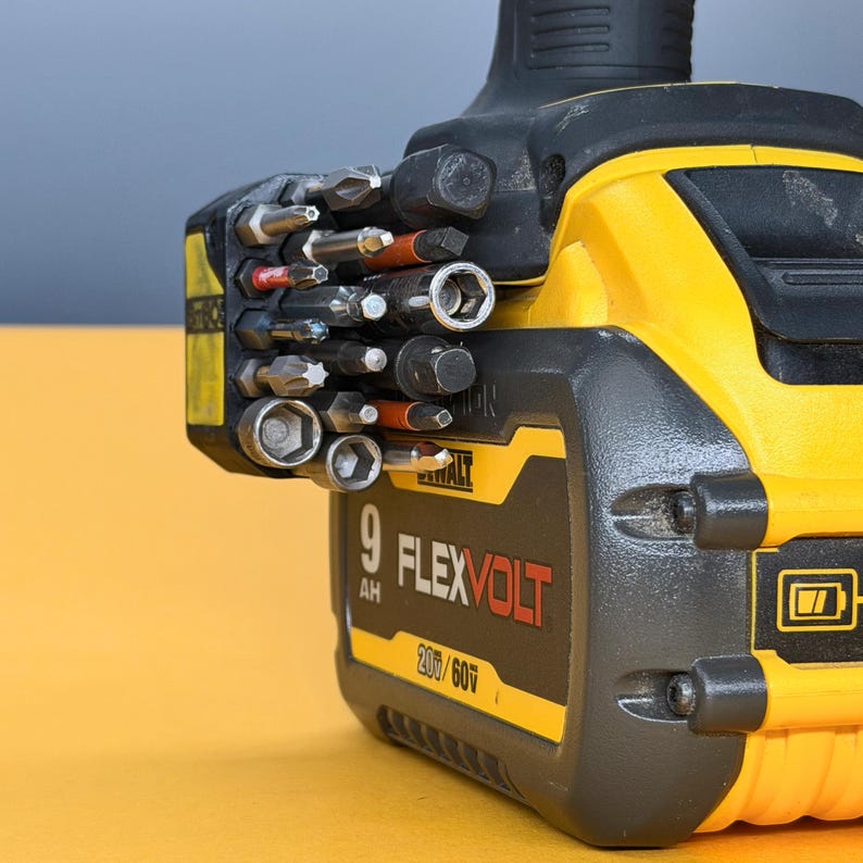 May include: A yellow and black DeWalt FlexVolt 9 AH battery pack with a side-mounted bit holder containing various metal screwdriver bits and sockets. The battery features the text 9 AH FLEXVOLT 20V/60V printed on the side in black and red.