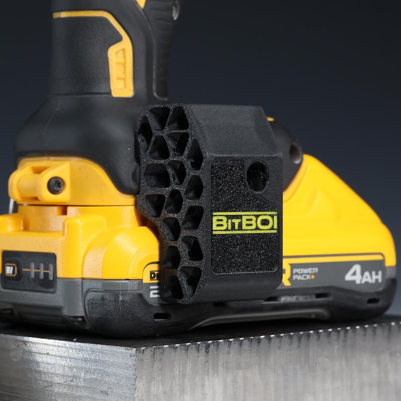 May include: A black 3D-printed BitBoi drill bit holder with a honeycomb side pattern attached to a yellow and black power tool battery. The holder features the text BitBoi in yellow lettering on the side, mounted on a 4Ah power pack battery.