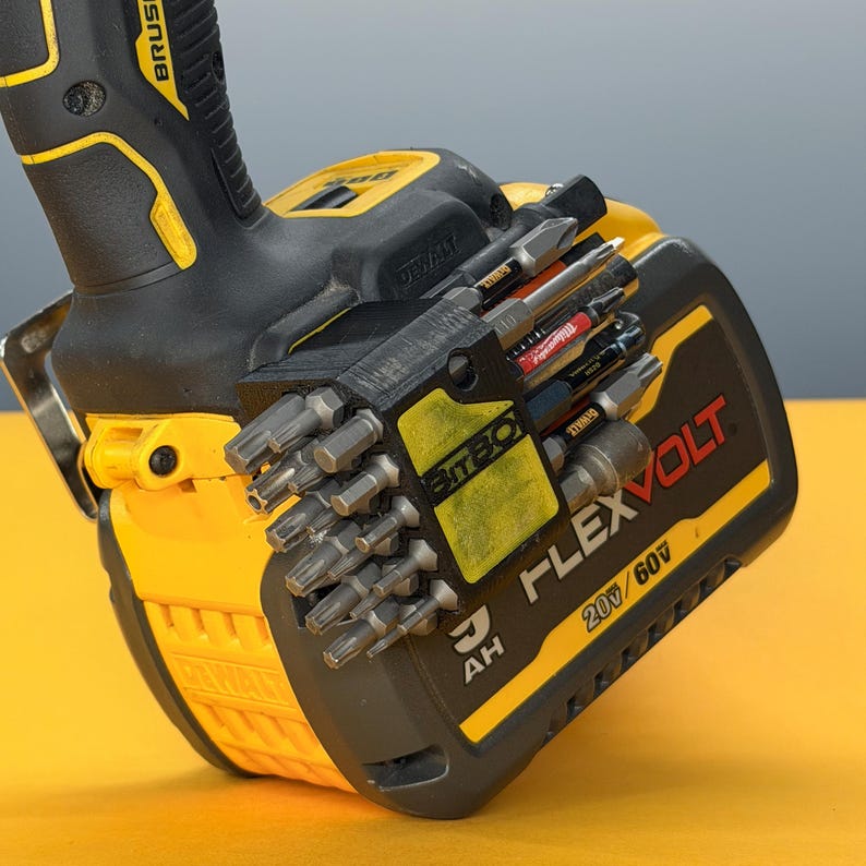 May include: A black 3D-printed bit holder attached to a yellow and black DeWalt FlexVolt 20V/60V battery pack. The holder contains multiple metal screwdriver bits and is mounted on the side of the battery, which is connected to a power tool handle.
