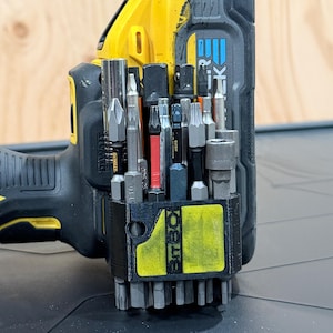 May include: A black 3D-printed BitBox bit holder attached to a yellow and black DeWalt power drill. The holder contains an assortment of metal screwdriver bits and socket adapters, including a T10 bit and a red-banded bit, organised in vertical slots.
