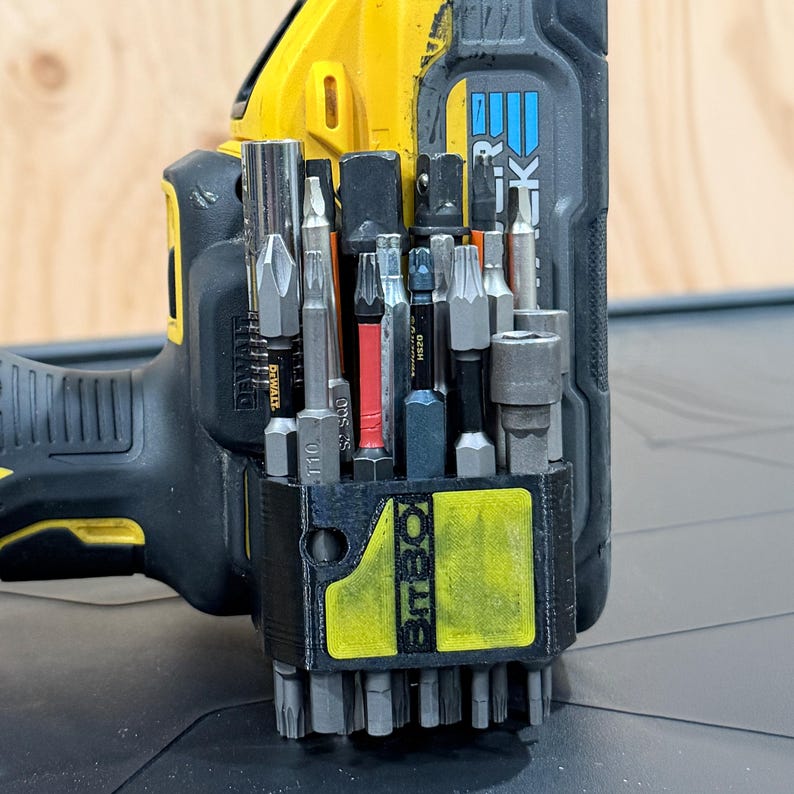 May include: A black 3D-printed BitBox bit holder attached to a yellow and black DeWalt power drill. The holder contains an assortment of metal screwdriver bits and socket adapters, including a T10 bit and a red-banded bit, organised in vertical slots.