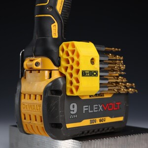 May include: A yellow and black DeWalt FlexVolt 9 AH 20V/60V battery pack attached to a power tool. A yellow, honeycomb-patterned BitBox drill bit holder is mounted to the side, containing a collection of gold-coloured metal drill bits.