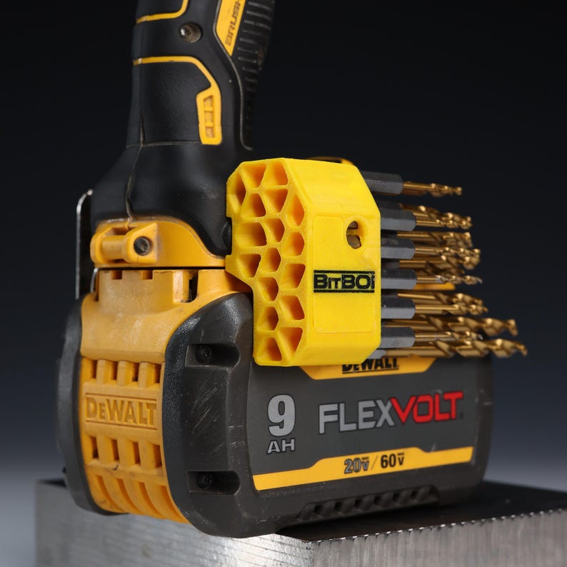 May include: A yellow and black DeWalt FlexVolt 9 AH 20V/60V battery pack attached to a power tool. A yellow, honeycomb-patterned BitBox drill bit holder is mounted to the side, containing a collection of gold-coloured metal drill bits.
