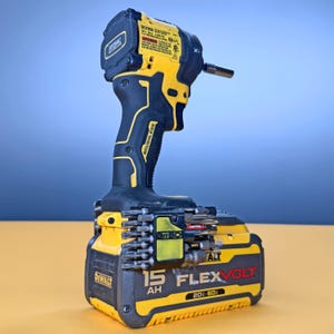 May include: A yellow and black DeWalt Atomic brushless impact driver attached to a 15 Ah FlexVolt 20V/60V battery pack. A black plastic bit holder is mounted to the battery, containing several metal screwdriver bits of various sizes and types.