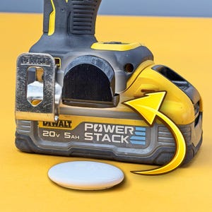 May include: A close-up of a black and yellow DeWalt Power Stack 20V 5Ah battery pack with a white oval object on a yellow background. The battery pack has the text "DeWalt" and "Power Stack" printed on it.