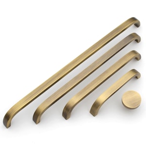 May include: A collection of antique brass cabinet hardware, including four pull handles of varying lengths and a round knob. The hardware has a curved design and a warm, aged finish, suitable for furniture restoration or new builds.