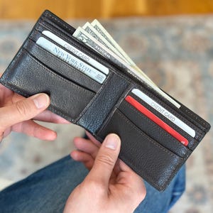 May include: A brown leather wallet with a credit card and cash inside. The wallet is open and the cash is sticking out of the top. The wallet has a flap that closes with a snap.