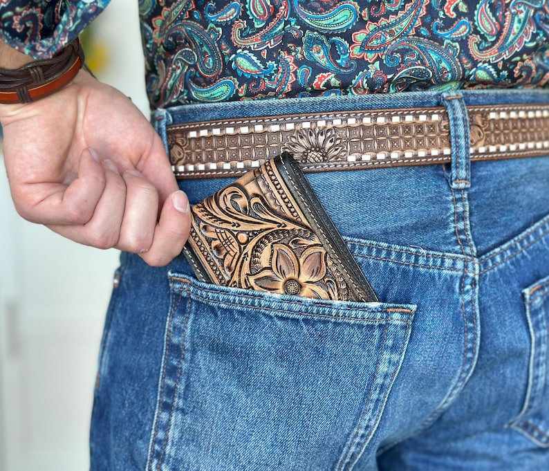 May include: A brown leather wallet with a floral design is tucked into the back pocket of a pair of blue jeans.