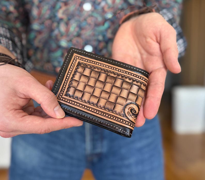 May include: A brown leather wallet with a tooled design and a black border. The wallet is closed and has a stitched edge.