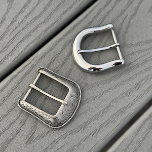 May include: Two silver belt buckles. One buckle is plain and the other has an engraved floral design.