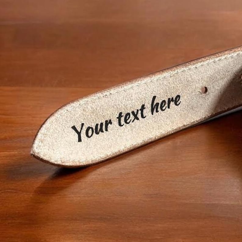 以下が含まれることがあります： 薄い茶色の革製のベルトのクローズアップ。ベルトには「Your text here」という文字が刻まれています。
