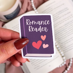 Op de afbeelding: Een paarse boek sticker met de tekst "Romance Reader" en drie roze harten.