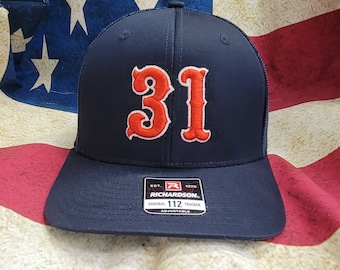 May include: A navy blue trucker hat with a red and white embroidered "31" on the front. The hat has a mesh back and a black adjustable strap with a "Richardson" label.