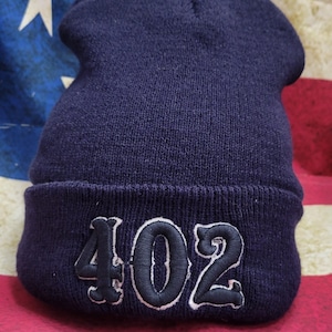 May include: A navy blue beanie with a white outline and the number "402" embroidered in black.