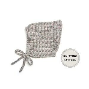 Puede incluir: Un gorro de bebé de punto gris con un lazo. El gorro tiene un patrón texturizado y está hecho con un hilo moteado. El texto "Knitting Pattern" es visible en un círculo en el lado derecho de la imagen.