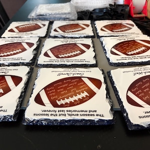 Puede incluir: Una colecci&oacute;n de posavasos cuadrados de pizarra con bordes irregulares. Cada posavasos presenta un gr&aacute;fico de un bal&oacute;n de f&uacute;tbol americano, una lista de nombres, el texto 'The season ends, but the lessons and memories last forever.' y el nombre de un entrenador.