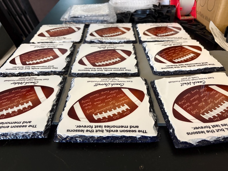 Puede incluir: Una colecci&oacute;n de posavasos cuadrados de pizarra con bordes irregulares. Cada posavasos presenta un gr&aacute;fico de un bal&oacute;n de f&uacute;tbol americano, una lista de nombres, el texto 'The season ends, but the lessons and memories last forever.' y el nombre de un entrenador.