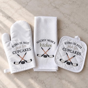 May include: A white oven mitt, a waffle-textured kitchen towel, and a square pot holder. The mitt and pot holder feature the text "ICING IS NOT just for CUPCAKES" with crossed hockey sticks and a puck. The towel says "HOCKEY MOM'S kitchen".