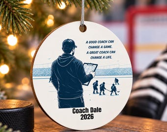 Puede incluir: Un adorno redondo blanco con el gráfico de un entrenador de hockey sosteniendo una carpeta, con el texto: A GOOD COACH CAN CHANGE A GAME. A GREAT COACH CAN CHANGE A LIFE. COACH DALE 2026. El diseño incluye una pista de hockey y jugadores.