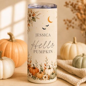 May include: A cylindrical tumbler with a cream-coloured background featuring a floral and pumpkin print. The text reads JESSICA Hello PUMPKIN. The design includes a crescent moon, two small bats, and various autumn-themed botanical elements.