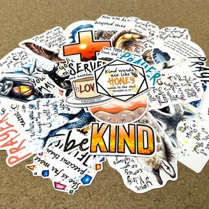 May include: A collection of colorful stickers with inspirational quotes and images. The stickers feature a variety of designs, including a deer, a bee, a cross, a wolf, and a honeycomb. The stickers are printed on white paper and have a glossy finish.