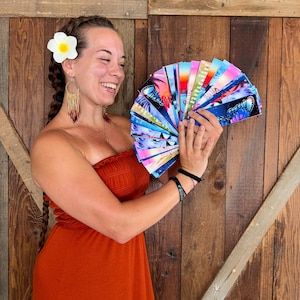 May include: A collection of rectangular bookmarks fanned out in a hand, featuring vibrant graphic designs including butterflies, sunset gradients, and inspirational text. Each bookmark displays a unique, colourful illustration with glossy finishes.