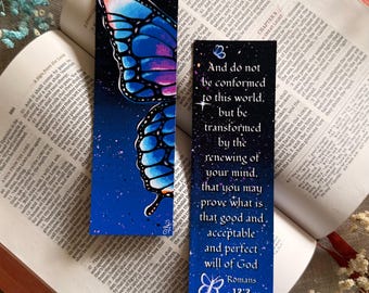 May include: Two rectangular bookmarks featuring a dark blue, starry night sky background. One bookmark displays a large, vibrant blue and pink butterfly wing. The other features white text reading, And do not be conformed to this world, but be transformed by the renewing of your mind, that you may prove what is that good and, acceptable and perfect will of God Romans 12:2, with small white butterfly illustrations.