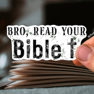 May include: A white sticker with black text that reads "BRO, READ YOUR Bible" with a black cross next to the word "Bible". The sticker is placed on a stack of books.