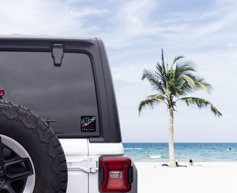 以下が含まれることがあります： 車の窓に貼られた、"HEAT"の文字と上向きと下向きの矢印が描かれた白黒のステッカー。ステッカーには「I May Persist」の文字も含まれています。背景には、ヤシの木と海のあるビーチが写っています。