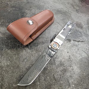 May include: A folding knife with a patterned blade and a brown leather sheath. The knife blade has a unique swirling pattern. The sheath is closed with a silver snap.