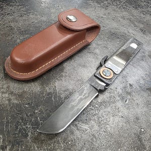 May include: A white ceramic mug with a black handle and the text "But First, Coffee" in a bold, black font. The mug is set against a blurred background, suggesting a cozy setting.