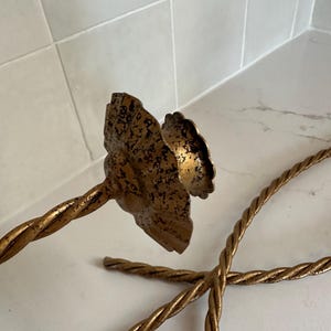 K&ouml;nnte beinhalten: Ein Paar goldene Kerzenhalter aus Metall mit einem gedrehten Seil-Design. Die Kerzenhalter haben eine dekorative, blumenf&ouml;rmige Oberseite.