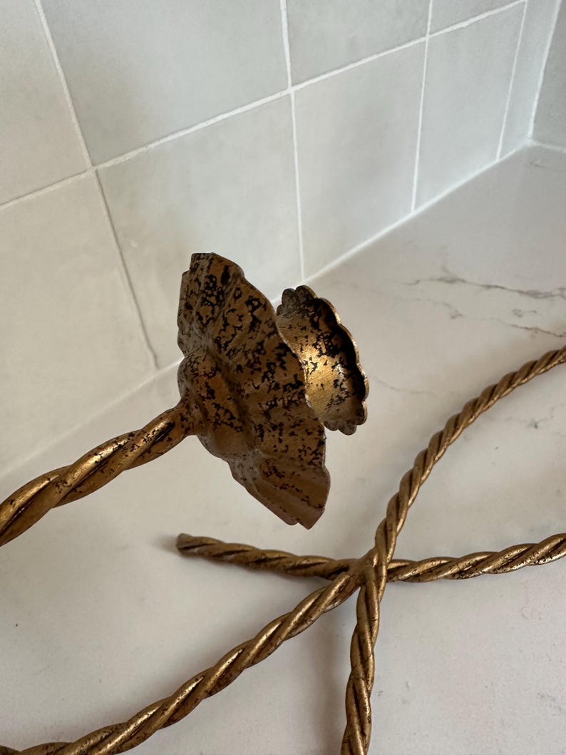 K&ouml;nnte beinhalten: Ein Paar goldene Kerzenhalter aus Metall mit einem gedrehten Seil-Design. Die Kerzenhalter haben eine dekorative, blumenf&ouml;rmige Oberseite.