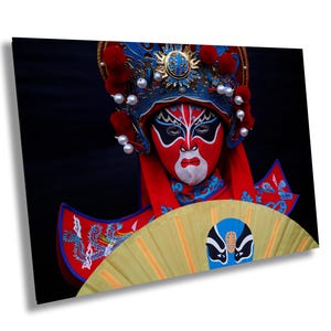 May include: A performer in a traditional Chinese opera costume with a red and blue headdress, a red and blue robe, and a yellow hand fan. The performer has elaborate white and red makeup on their face.