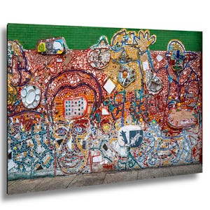 May include: A vibrant mosaic mural featuring a variety of colorful tiles. The artwork depicts abstract figures, faces, and shapes in shades of red, orange, yellow, blue, and white. The mural is set against a green brick background.