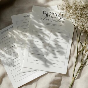 May include: Three printable bridal shower game cards with the title "Bridal Charades" and instructions to "Cut out the words below and place them into a bowl. For every guest to draw."